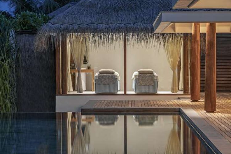 Exterior view of spa treatment room across swimming pool at Two Bedroom Beach Pool Residence at dusk